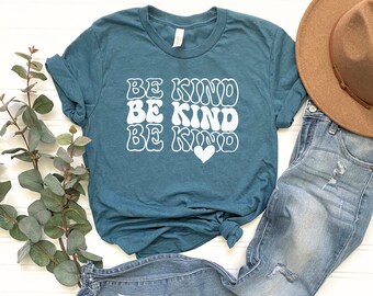 May include: Teal blue t-shirt with a white graphic that says "Be Kind" three times in a retro font with a white heart at the bottom.