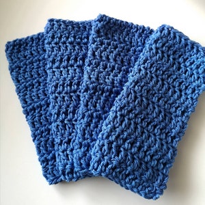 May include: A set of four rectangular blue dishcloths featuring a consistent crochet stitch pattern. Each cloth is crafted from a medium blue yarn, displaying a textured, woven appearance with visible loops throughout the entire surface area.