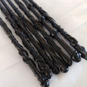 May include: A set of eight black wooden wands with intricate designs and different tip styles. The wands are arranged in a row, with the tips pointing in different directions.