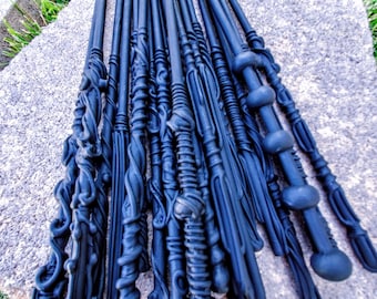 May include: A collection of black, intricately designed wands, likely made of wood or plastic, arranged on a gray stone surface. The wands are all different shapes and sizes, with some having a more ornate design than others.
