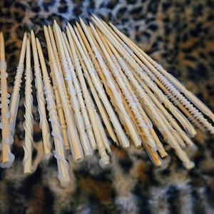 May include: A collection of wooden wands with white, translucent, decorative accents. The wands are arranged in a fan shape on a brown and white patterned surface.