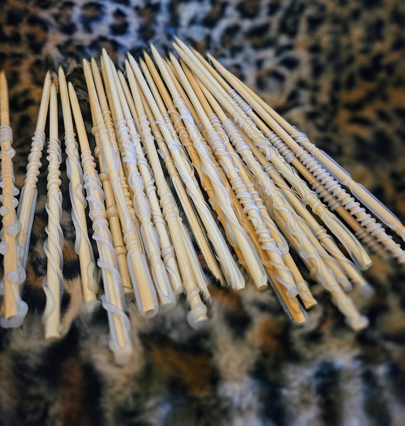 May include: A collection of wooden wands with white, translucent, decorative accents. The wands are arranged in a fan shape on a brown and white patterned surface.