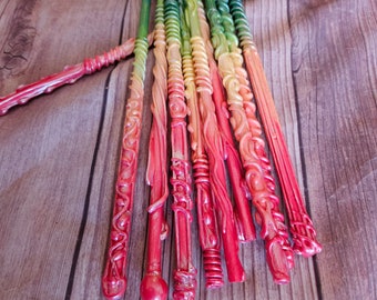 May include: A collection of colorful, hand-painted wooden wands with intricate details. The wands are arranged in a fan shape, with the tips pointing towards the top of the image. The wands are painted in shades of red, orange, yellow, green, blue, and purple.