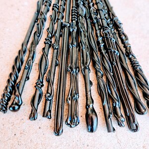 May include: A collection of black wands with various ornate designs. The wands have twisted, swirling, and textured patterns. The wands are arranged in a fan shape, with the tips pointing upwards. The wands are made of a shiny, dark material.