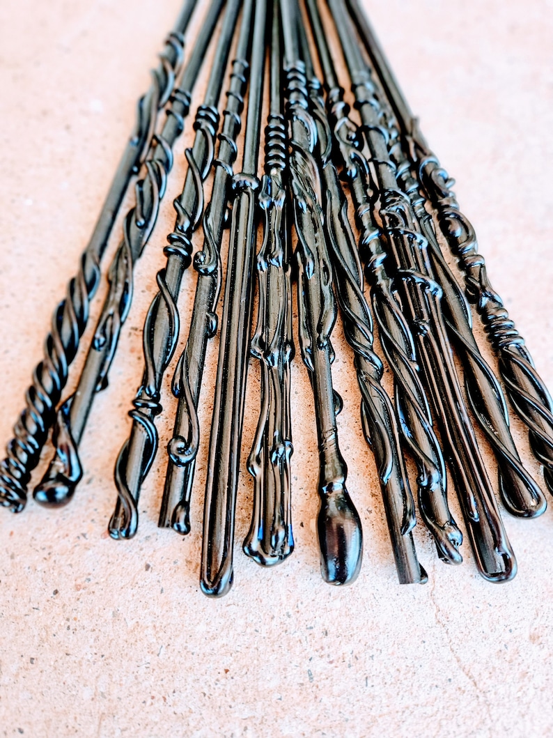 May include: A collection of black wands with various ornate designs. The wands have twisted, swirling, and textured patterns. The wands are arranged in a fan shape, with the tips pointing upwards. The wands are made of a shiny, dark material.