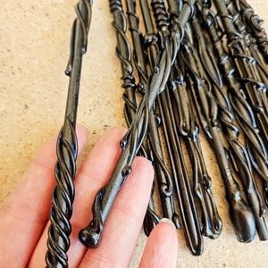 May include: A collection of black wands with intricate, swirling designs. The wands have a glossy finish and vary in their decorative elements, with some featuring twisted patterns and others smooth, bulbous ends. The wands are displayed against a neutral background.