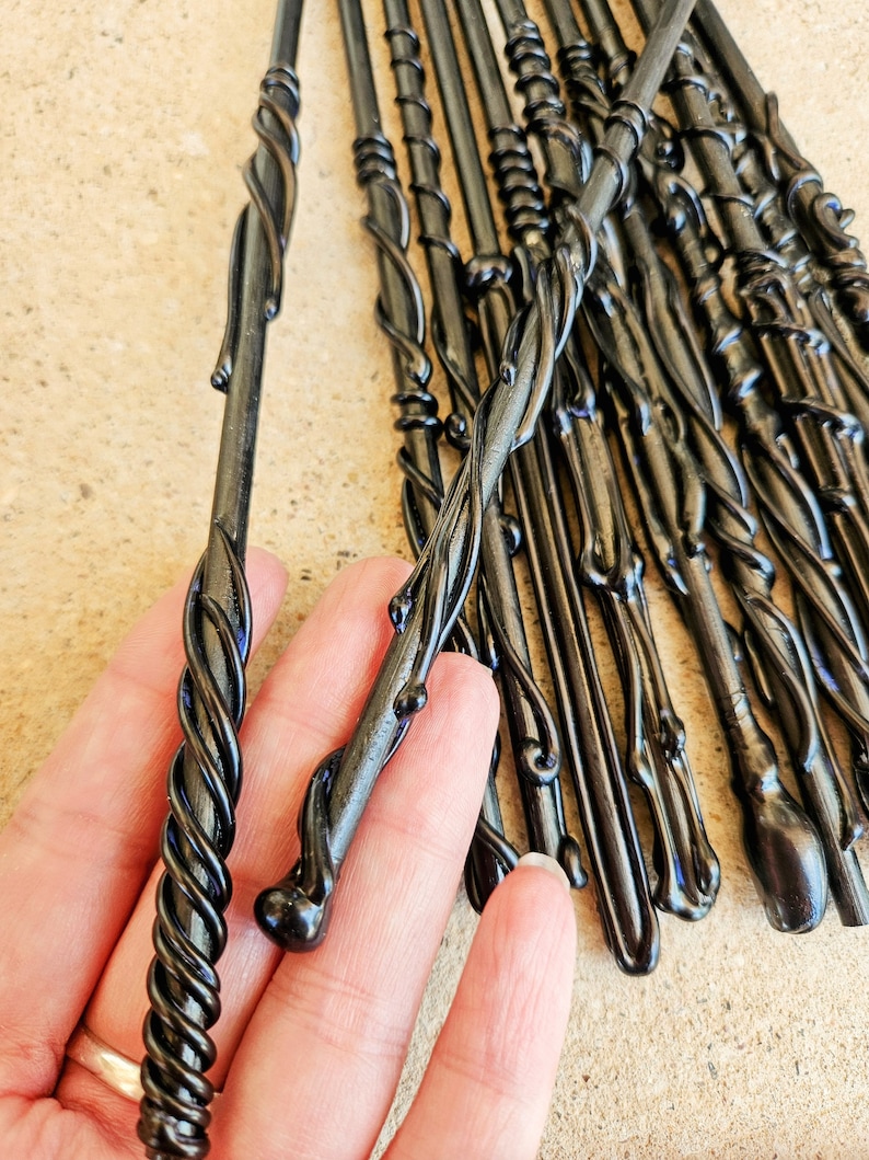 May include: A collection of black wands with intricate, swirling designs. The wands have a glossy finish and vary in their decorative elements, with some featuring twisted patterns and others smooth, bulbous ends. The wands are displayed against a neutral background.