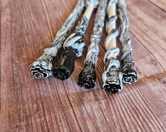 May include: Five black and white painted wooden wands with black rose-shaped ends. The wands are arranged in a fan shape on a wooden surface.