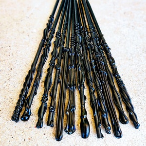 May include: A collection of black wands with various designs, including twisted, smooth, and ornate styles. The wands are arranged in a fan shape, showcasing their different shapes and textures. The wands are made of a glossy material.