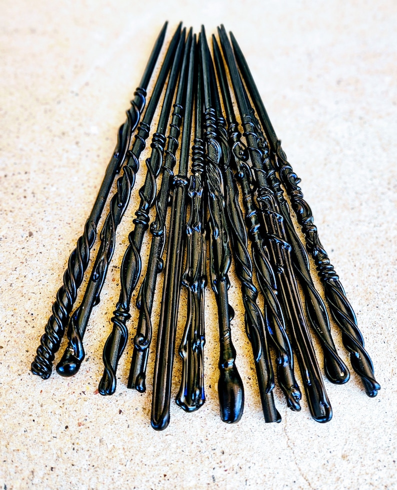 May include: A collection of black wands with various designs, including twisted, smooth, and ornate styles. The wands are arranged in a fan shape, showcasing their different shapes and textures. The wands are made of a glossy material.