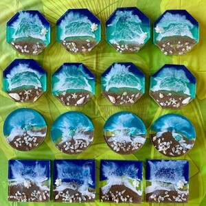 May include: Set of 15 resin coasters featuring a beach scene with blue and white waves, brown sand, and white seashells. The coasters are in various shapes, including octagons and circles.