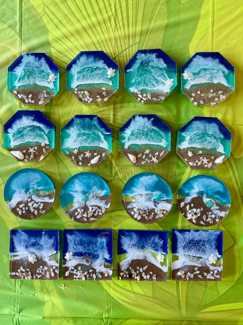 May include: Set of 15 resin coasters featuring a beach scene with blue and white waves, brown sand, and white seashells. The coasters are in various shapes, including octagons and circles.