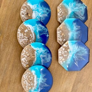 May include: Set of six resin coasters featuring a beach scene with blue, white, and brown colors. The coasters are round and octagonal.
