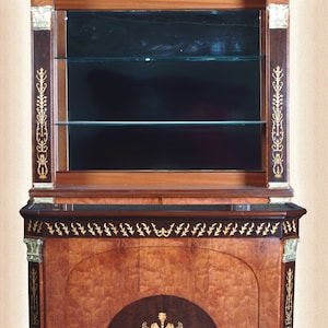 May include: A mahogany wood cabinet with glass shelves and gold accents. The cabinet has a decorative design on the front with a gold trim and a black marble top.