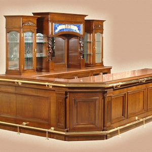 May include: A large, wooden bar with a curved front and a back bar with glass shelves. The bar has a brass rail and a brass footrest. The back bar has a stained glass window with the words "The Bar" in the center.