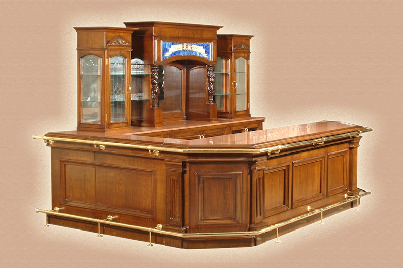 May include: A large, wooden bar with a curved front and a back bar with glass shelves. The bar has a brass rail and a brass footrest. The back bar has a stained glass window with the words "The Bar" in the center.