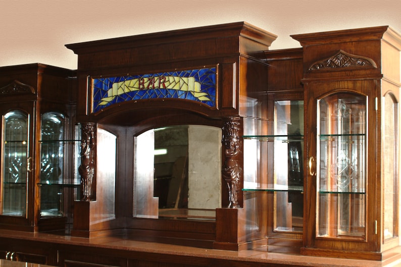 May include: A wooden bar unit with a stained glass window that says "BAR" above a mirror. The unit has glass shelves and doors with etched glass.