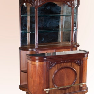 May include: A dark wood bar cabinet with a glass-front top section and a lower cabinet with a rounded front. The top section has a mirrored back and two shelves. The lower cabinet has a black countertop and a decorative oval panel on the front.