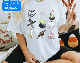 Op de afbeelding: Wit T-shirt met een Halloween-thema. De illustraties omvatten vleermuizen, een spinnenweb, een heksenhoed, een ketel, een spook, een drankfles, een raaf en kaarsen. De woorden "original designer" en ".png download" zijn zichtbaar.
