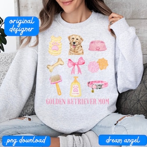 May include: A light grey sweatshirt with the text "Golden Retriever Mom" in pink lettering. The sweatshirt features a watercolour illustration of a golden retriever dog, a bone, a dog collar, a dog brush, a dog toy, a dog bowl, a dog vest, a pink bow, and a bottle of shampoo.