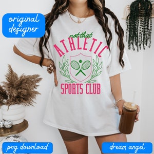 May include: White t-shirt with a green and pink graphic that says "Not That Athletic Sports Club" with a tennis racket and ball design.