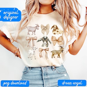 May include: A white t-shirt with a design of watercolor goats and bows. The goats are brown, white, and black. The bows are brown and beige.