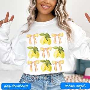 May include: White sweatshirt with a lemon and bow pattern. The lemons are yellow with green leaves and the bows are pink and yellow.
