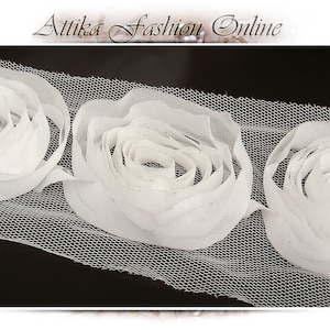 May include: White fabric trim with three dimensional flower embellishments. The trim is made of a sheer mesh fabric with white fabric flowers.