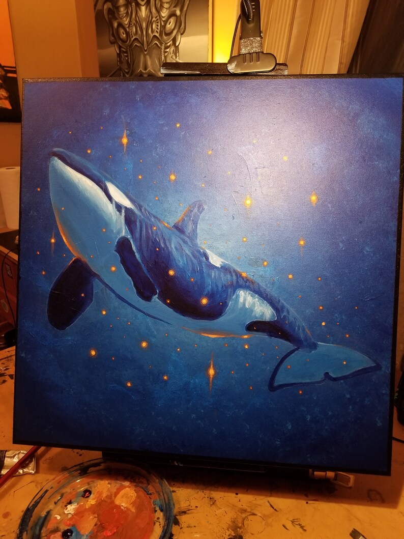 May include: A square canvas painting featuring an orca whale in a deep blue ocean. The whale is painted in blue and white, with glowing orange stars. The artwork evokes a sense of wonder and the vastness of the sea.