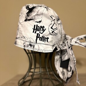 May include: A white and black patterned bandana with the words "Harry Potter" in black lettering. The bandana is on a metal stand.