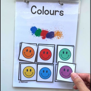 May include: A learning activity for children to match smiley faces to different colored squares. The squares are orange, red, green, yellow, blue, and purple. The title of the activity is "Colours".