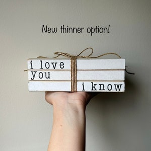 May include: A set of three white faux books stacked and tied with twine. The books are decorated with black text that reads "i love you" and "i know".