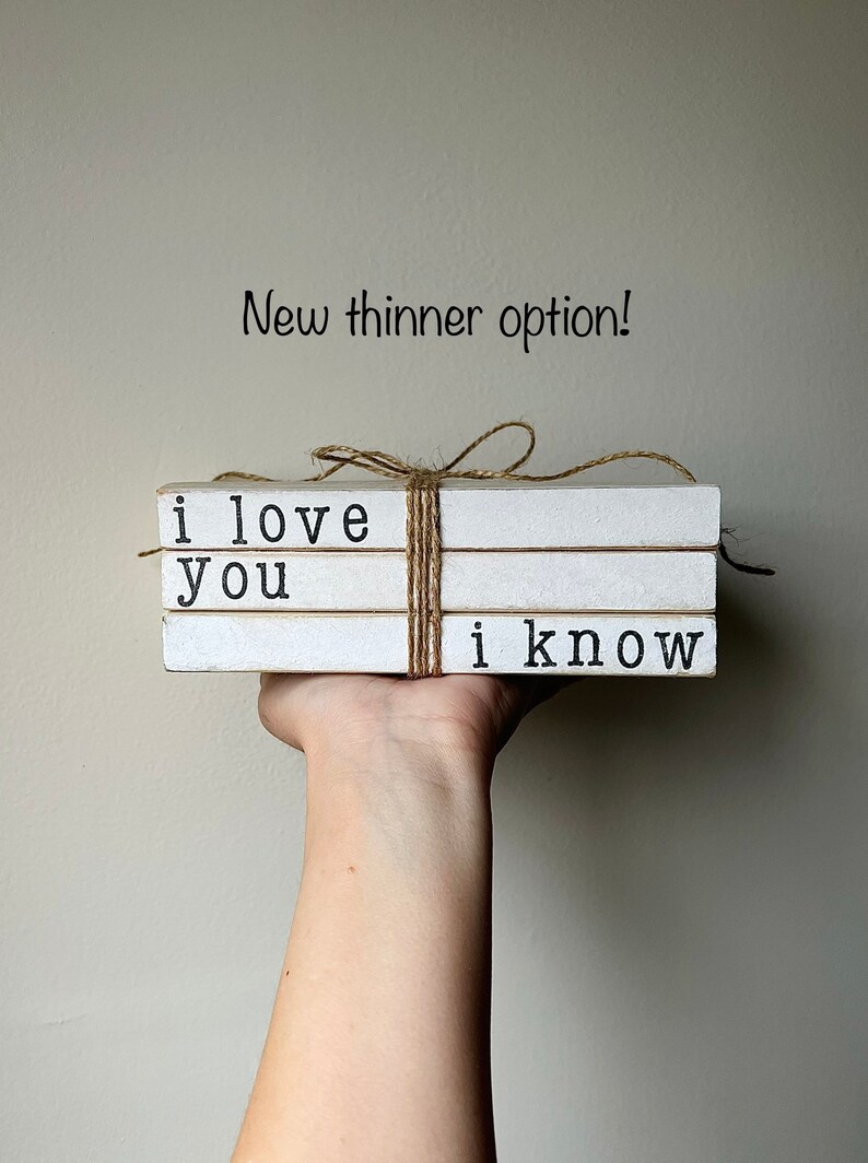 May include: A set of three white faux books stacked and tied with twine. The books are decorated with black text that reads "i love you" and "i know".