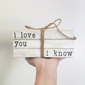 May include: A stack of three white books with black text. The top book says "i love", the middle book says "you", and the bottom book says "i know". The books are tied together with twine.