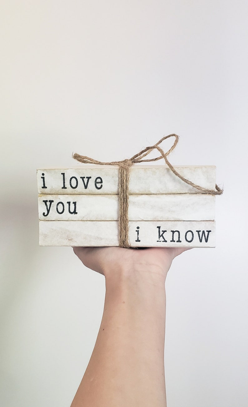 May include: A stack of three white books with black text. The top book says "i love", the middle book says "you", and the bottom book says "i know". The books are tied together with twine.