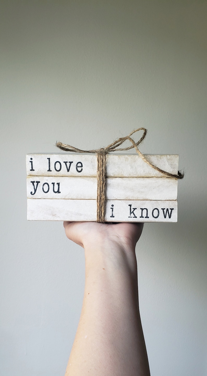 May include: A stack of three white books with black text. The books are tied together with twine and the text reads "i love you i know".