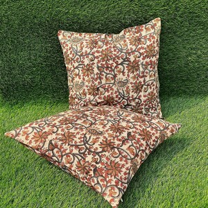 May include: Two cream-colored pillow covers with a floral pattern in shades of brown and orange. The floral pattern features intricate vines and leaves.