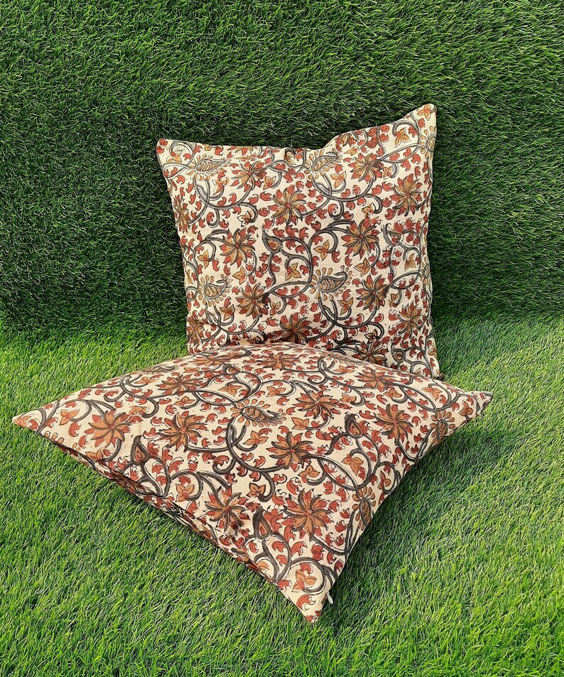 May include: Two cream-colored pillow covers with a floral pattern in shades of brown and orange. The floral pattern features intricate vines and leaves.