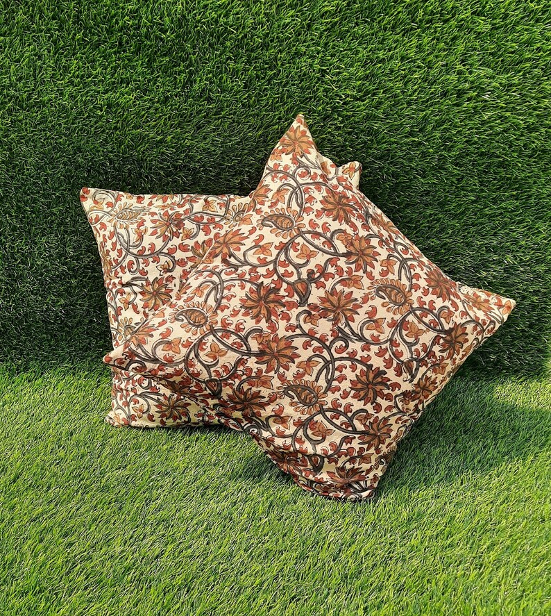 May include: Two decorative throw pillows with a floral pattern in shades of brown, cream, and black. The pillows are on a green grassy surface.