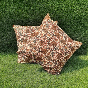 May include: Two decorative throw pillows with a floral pattern in shades of brown, cream, and black. The pillows are on a green grassy surface.