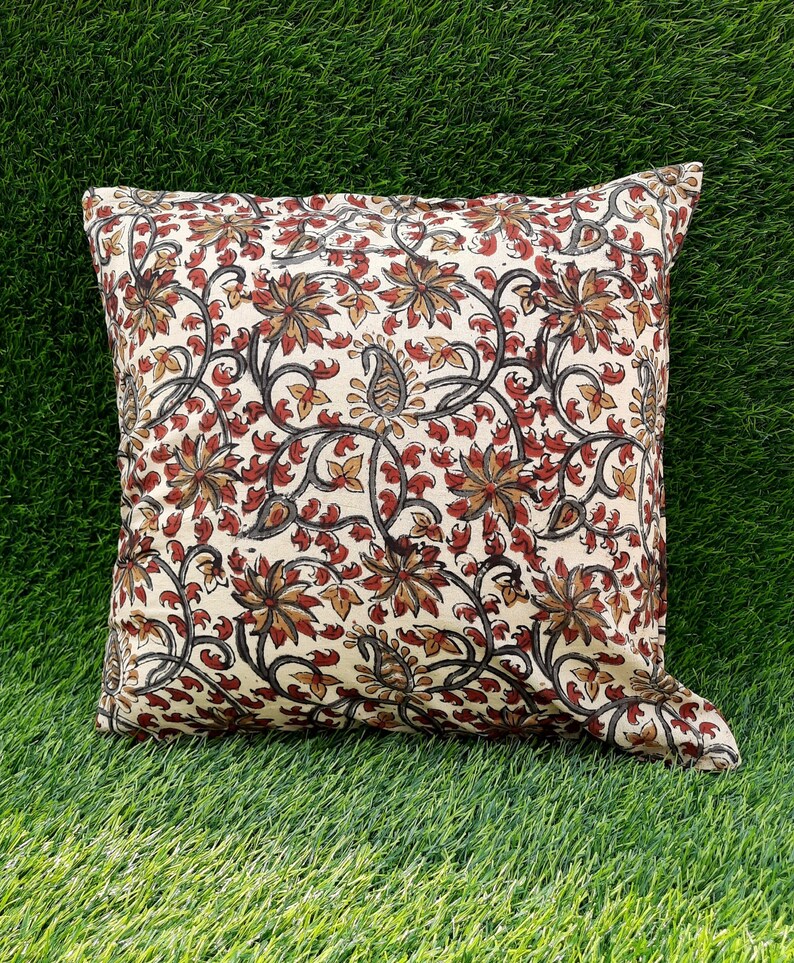 May include: A cream-colored throw pillow with a floral pattern in shades of red, brown, and black. The pillow is made of cotton and has a square shape.