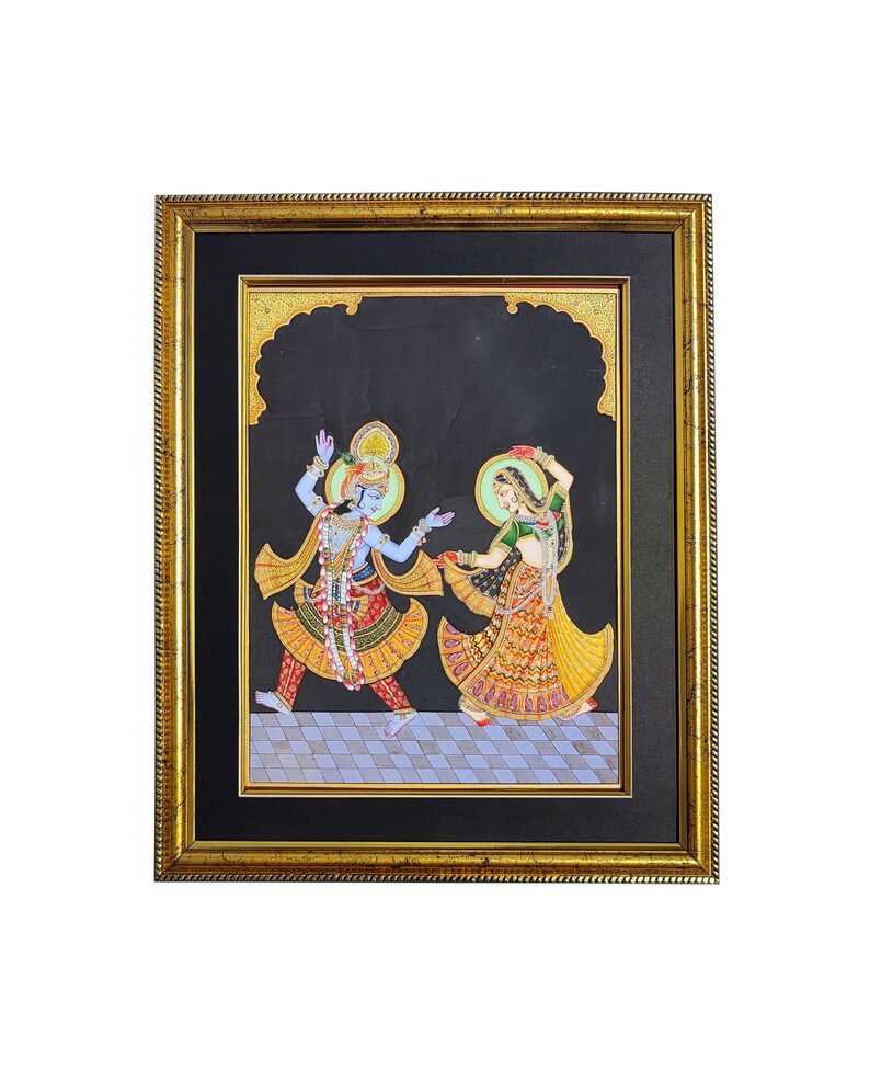 May include: A framed painting on a black background depicting two figures in traditional attire dancing on a checkered floor. The figure on the left has blue skin and wears a yellow and red outfit, while the figure on the right wears a green and yellow dress. Both figures have halos.