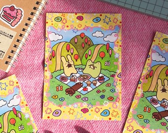 May include: Notebooks and stickers with a picnic theme. The notebooks have a spiral binding and are decorated with stickers of a frog, a cake, and a bear. The stickers are on a brown notebook. The image also shows a picnic scene with a rabbit and a frog.