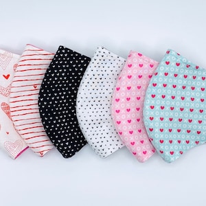May include: Six fabric face masks with different heart and XO patterns. The masks are in various colors, including white, black, pink, blue, and red.