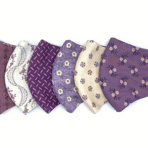 May include: Five purple and cream fabric face masks with different floral patterns.