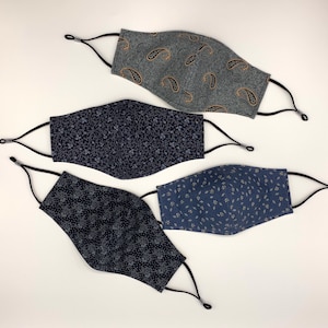 May include: Four fabric face masks with different patterns. The masks are all dark blue with white and gold patterns. The patterns include paisley, small flowers, and leaves.