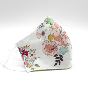 May include: A white face mask with a floral print featuring pink, red, and yellow flowers. The mask has white ties.
