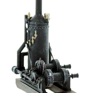 May include: A miniature black steam engine model with a tall smokestack, cylindrical boiler, and intricate mechanical details. The model sits on a rectangular wooden base, showcasing gears, pipes, and other components.