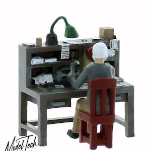 May include: A miniature model of a person sitting at a desk with a lamp, tools, and papers. The desk is made of wood and has a drawer. The person is wearing a gray shirt and a white hat. The chair is red.