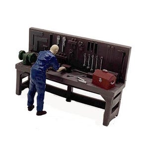 May include: A miniature model of a workbench with a figure of a person in blue overalls working on a project. The workbench has a variety of tools hanging on the wall behind it, including wrenches, screwdrivers, and a hammer. There is also a toolbox on the workbench.